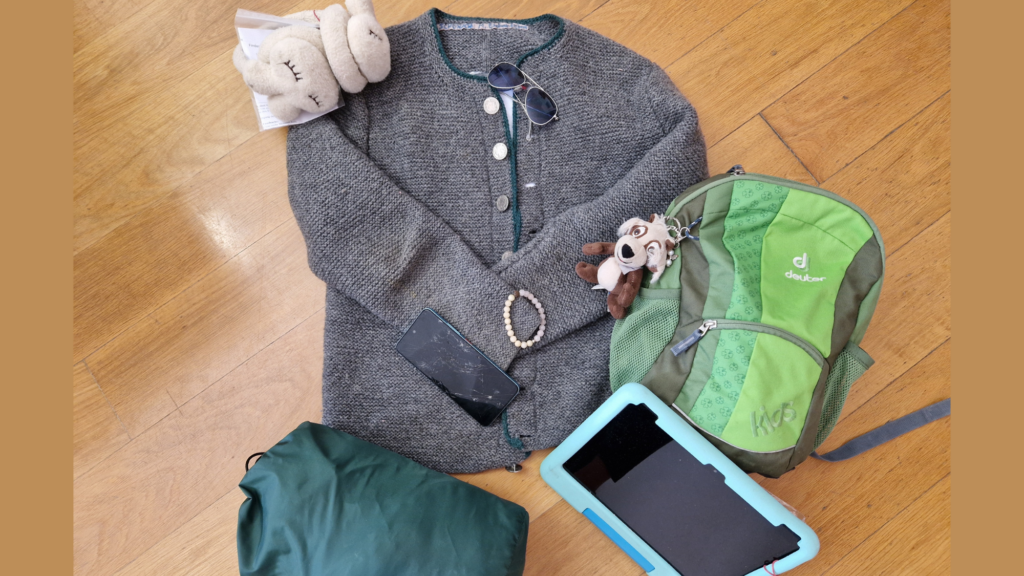 Fundsachenversteigerung 2026 - Es sind verschiedene Fundsachen zu sehen, die am Boden liegend arrangiert sind, z.B. eine Jacke, ein Kinderrucksack, ein Schlafsack und eine Sonnenbrille.