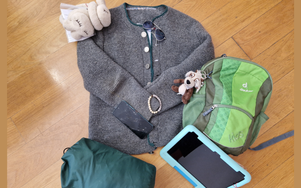 Fundsachenversteigerung 2026 - Es sind verschiedene Fundsachen zu sehen, die am Boden liegend arrangiert sind, z.B. eine Jacke, ein Kinderrucksack, ein Schlafsack und eine Sonnenbrille.