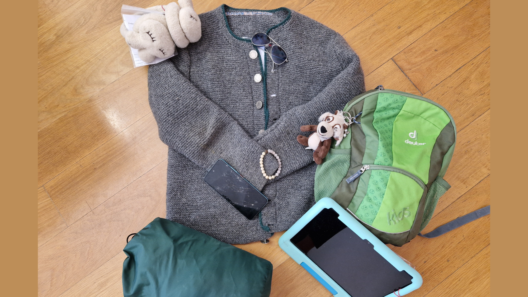 Fundsachenversteigerung 2026 - Es sind verschiedene Fundsachen zu sehen, die am Boden liegend arrangiert sind, z.B. eine Jacke, ein Kinderrucksack, ein Schlafsack und eine Sonnenbrille.