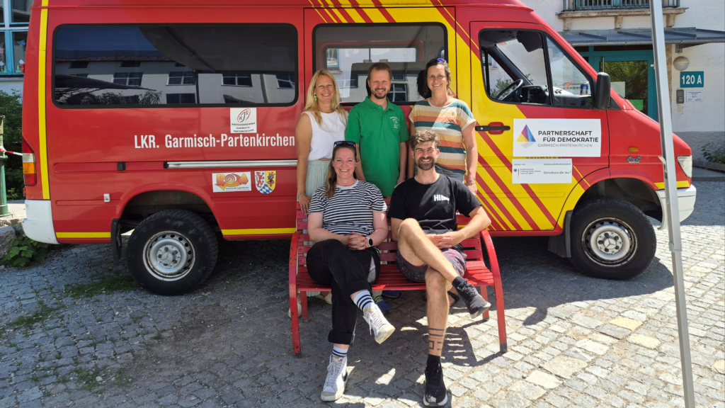 Demokratiemobil zu Gast an der James Loeb Grundschule. Fünf Personen stehen vor dem Demokratiemobil des Landkreises Garmisch-Partenkirchen
