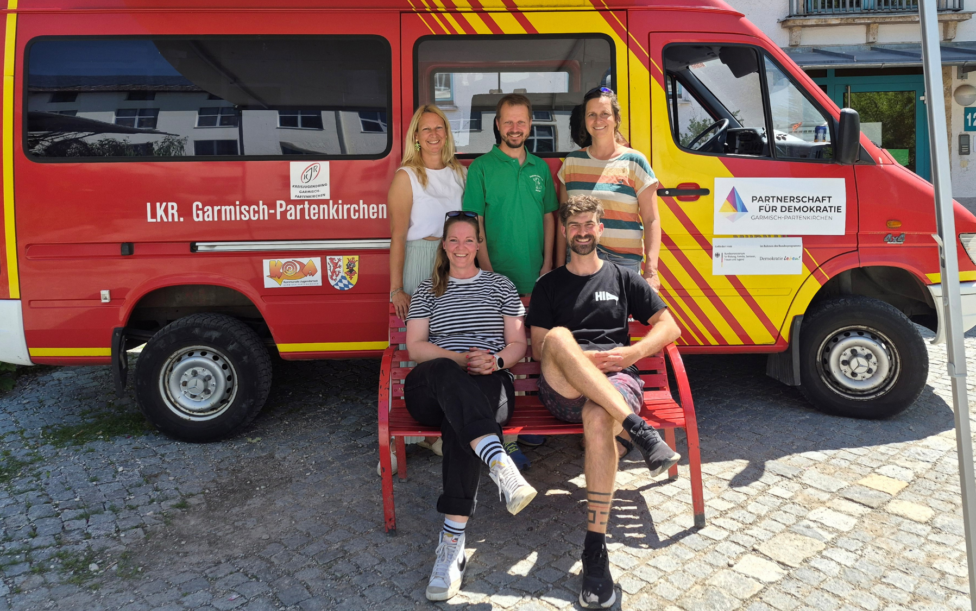 Demokratiemobil zu Gast an der James Loeb Grundschule. Fünf Personen stehen vor dem Demokratiemobil des Landkreises Garmisch-Partenkirchen