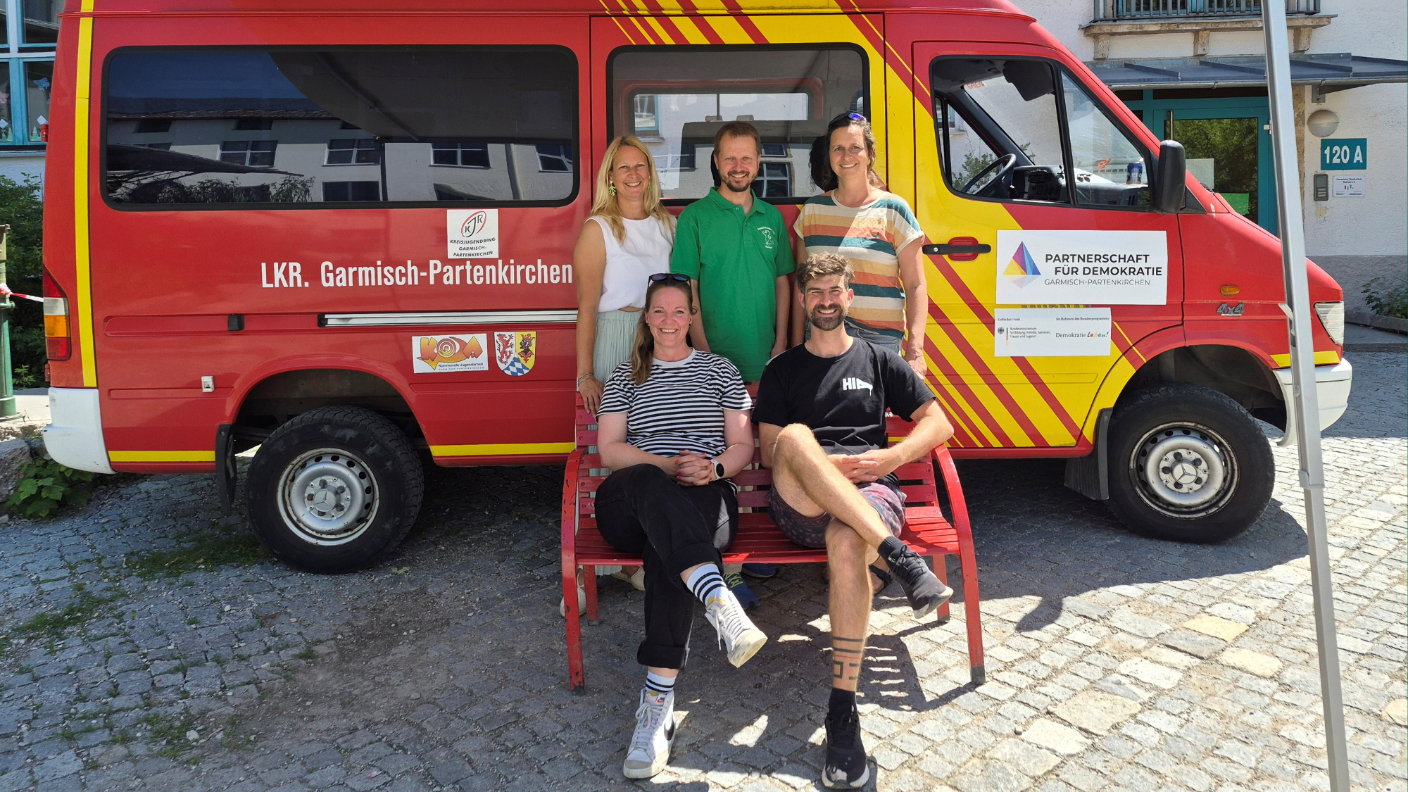 Demokratiemobil zu Gast an der James Loeb Grundschule. Fünf Personen stehen vor dem Demokratiemobil des Landkreises Garmisch-Partenkirchen