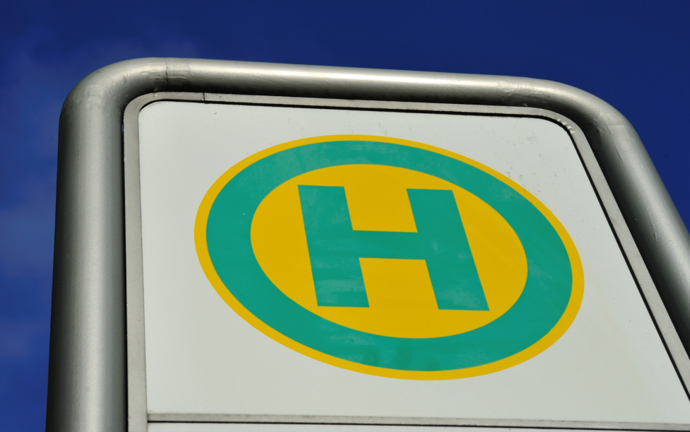 Bushaltestellenschild. Ein grünes H auf gelebn Hintergrund. Hinter dem Schild blauer Himmel.