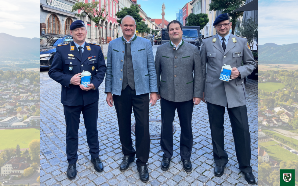 Kriegsgräberfürsorge 2026. Vier Männer, darunter zwei in Militäruniformen und zwei in zivilen Jacken, stehen lächelnd in der Murnauer Fußgängerzone und halten jeweils einen blauen Becher mit weißem Muster.